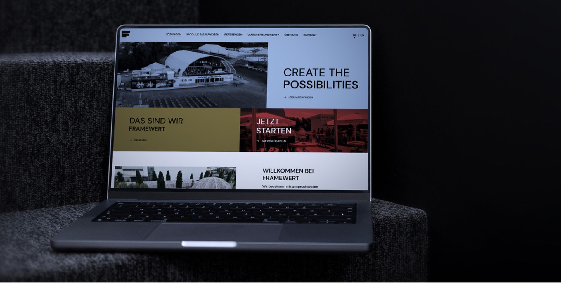 Laptop on a dark surface displaying a website with sections titled "Create the Possibilities," "Das sind wir," and "Jetzt starten."