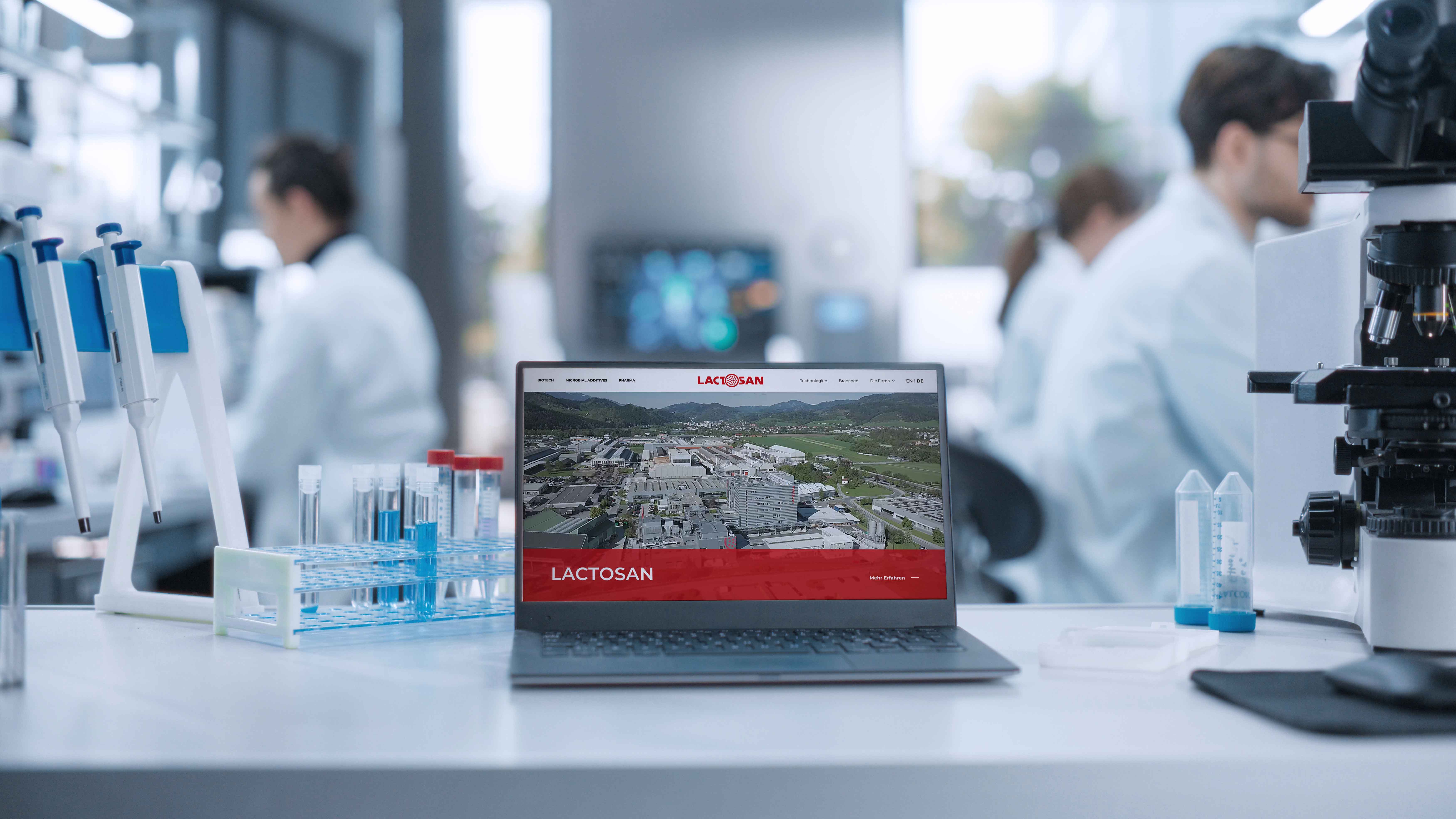 lx-media-case-studies-lactosan-website4 Laptop displaying a website on a lab table with test tubes and a microscope; scientists work in the blurred background.